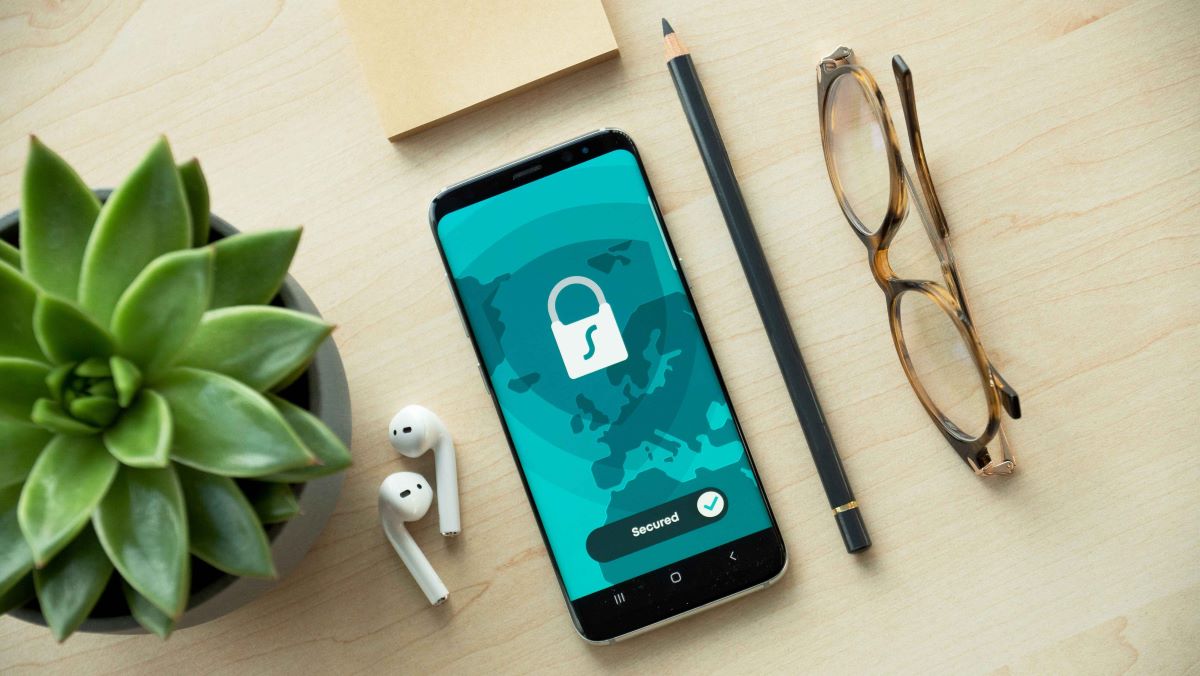 Phone on a desk next to a pen, glasses, plant and earpods