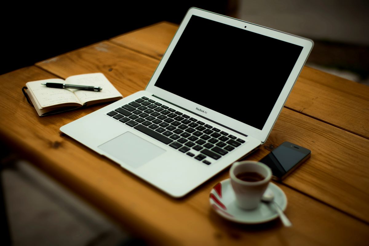 Laptop on a desk with a coffee mug and notepad on the side